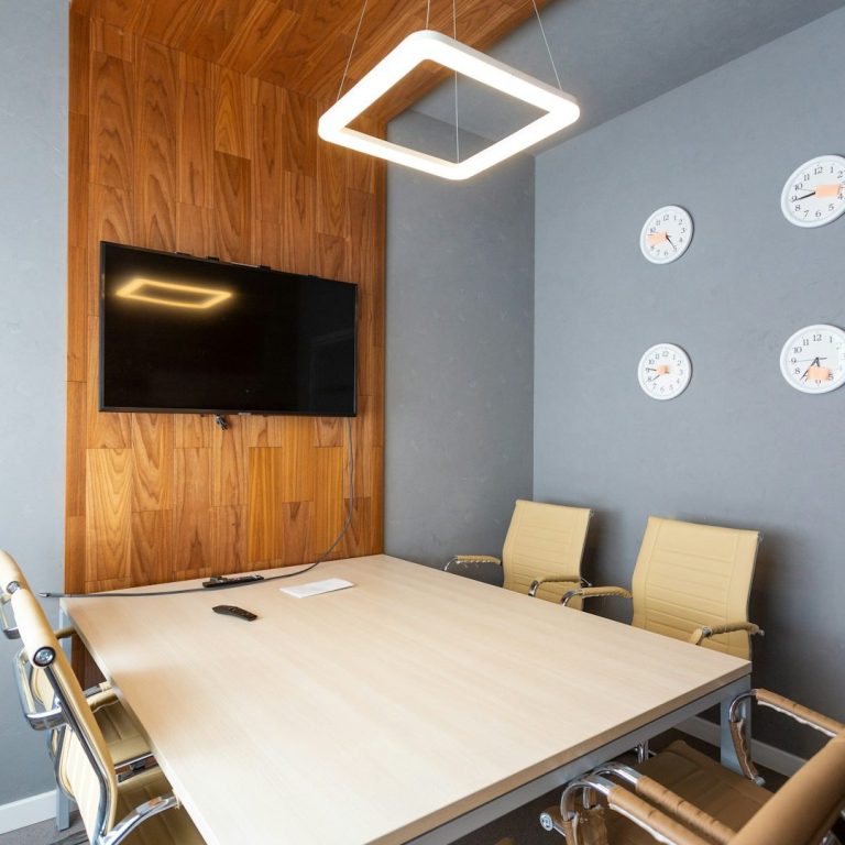 Moderne Konferenzraum mit Holzwänden, Tisch, Stühlen und Fernseher. Drei Uhren an der Wand. LED Beleuchtung im Büro