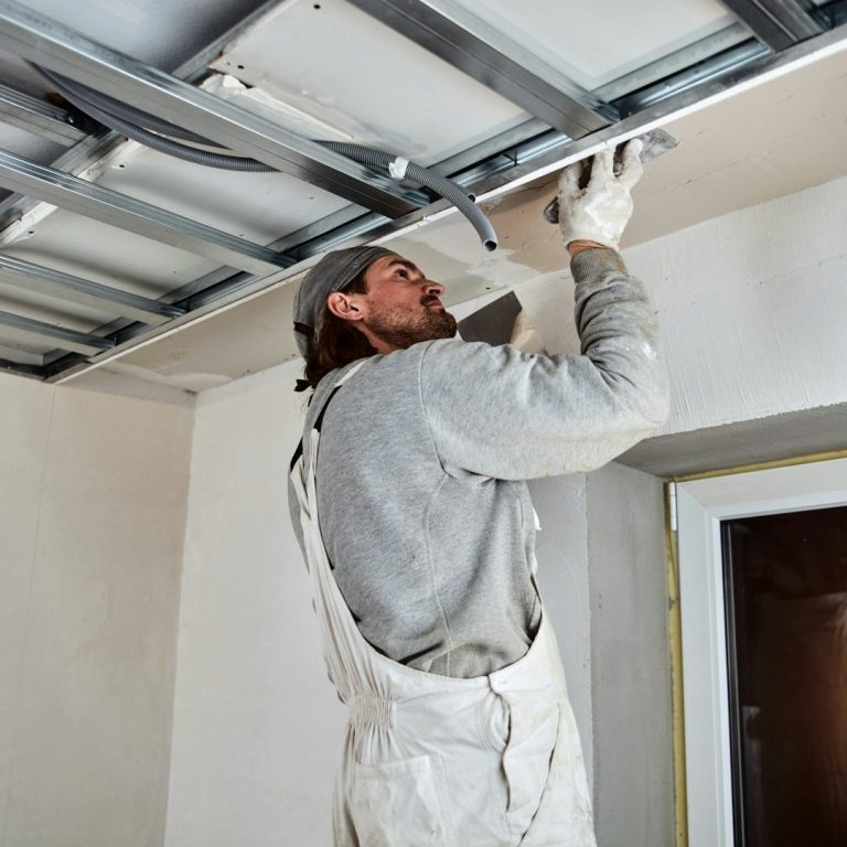 Handwerker spachtelt die Decke in einem Raum mit neuem Trockenbau. Installiert eine Rasterdecke