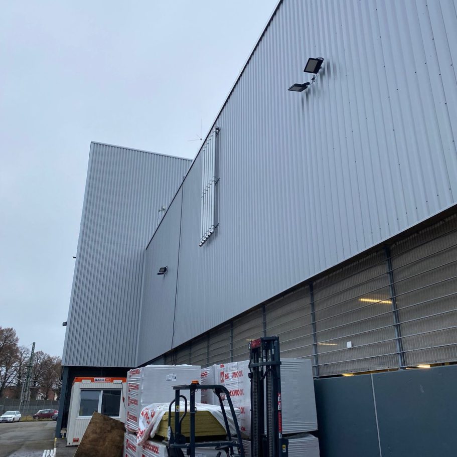 Fassade Trapezblech Ansicht einer grauen Lagergebäudewand aus Trapezblech mit Fenstern und einem Gabelstapler im Vordergrund.