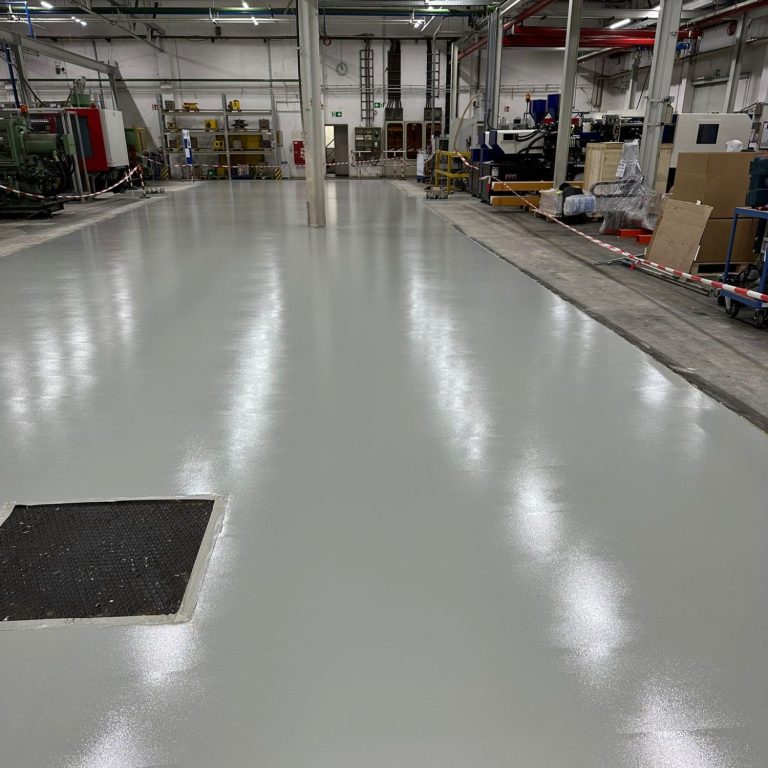 Helle, glatte Bodenbeschichtung in einer Industriehalle mit Lagereinrichtungen.