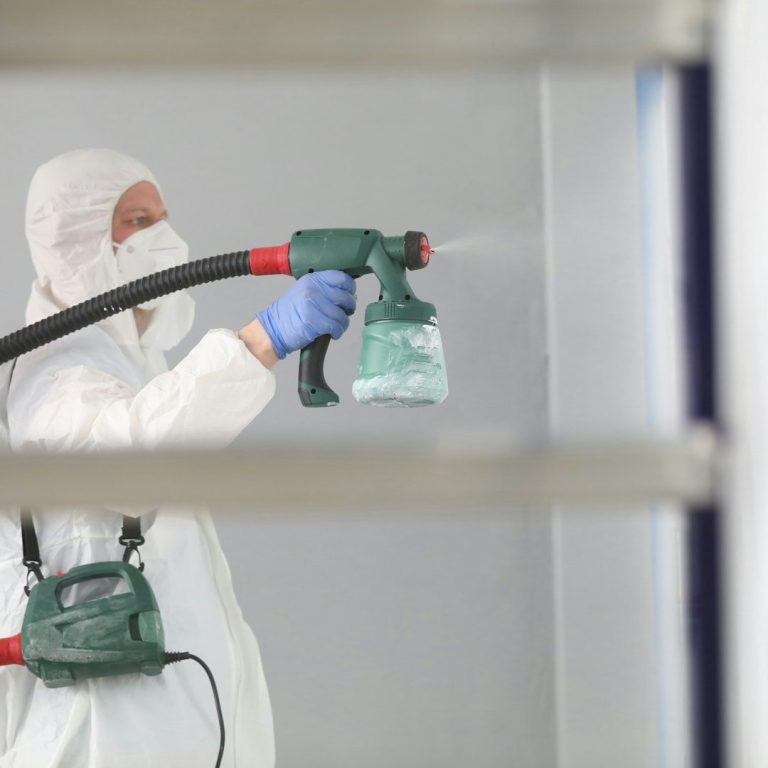 Person in Schutzkleidung sprüht Farbe an eine Wand mit einem Sprühgerät. Airless Spritzen, Malerarbeiten